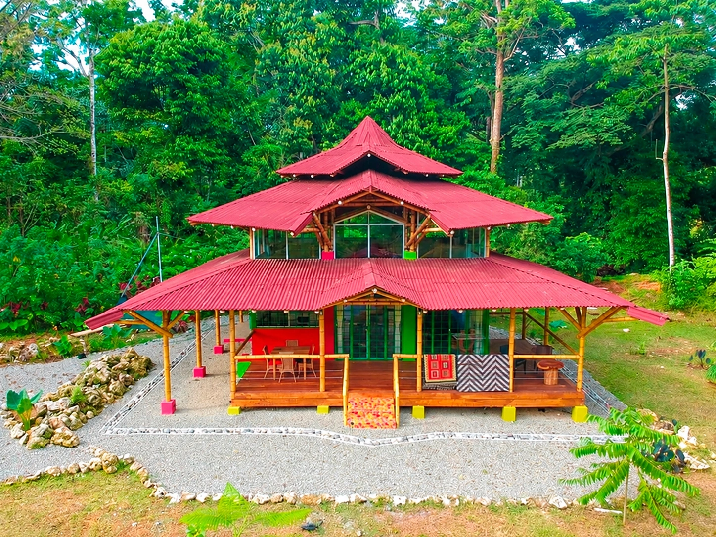 Fachada de Villa Nury, vivienda de bambú y madera con cubiertas rojas entre vegetación tropical